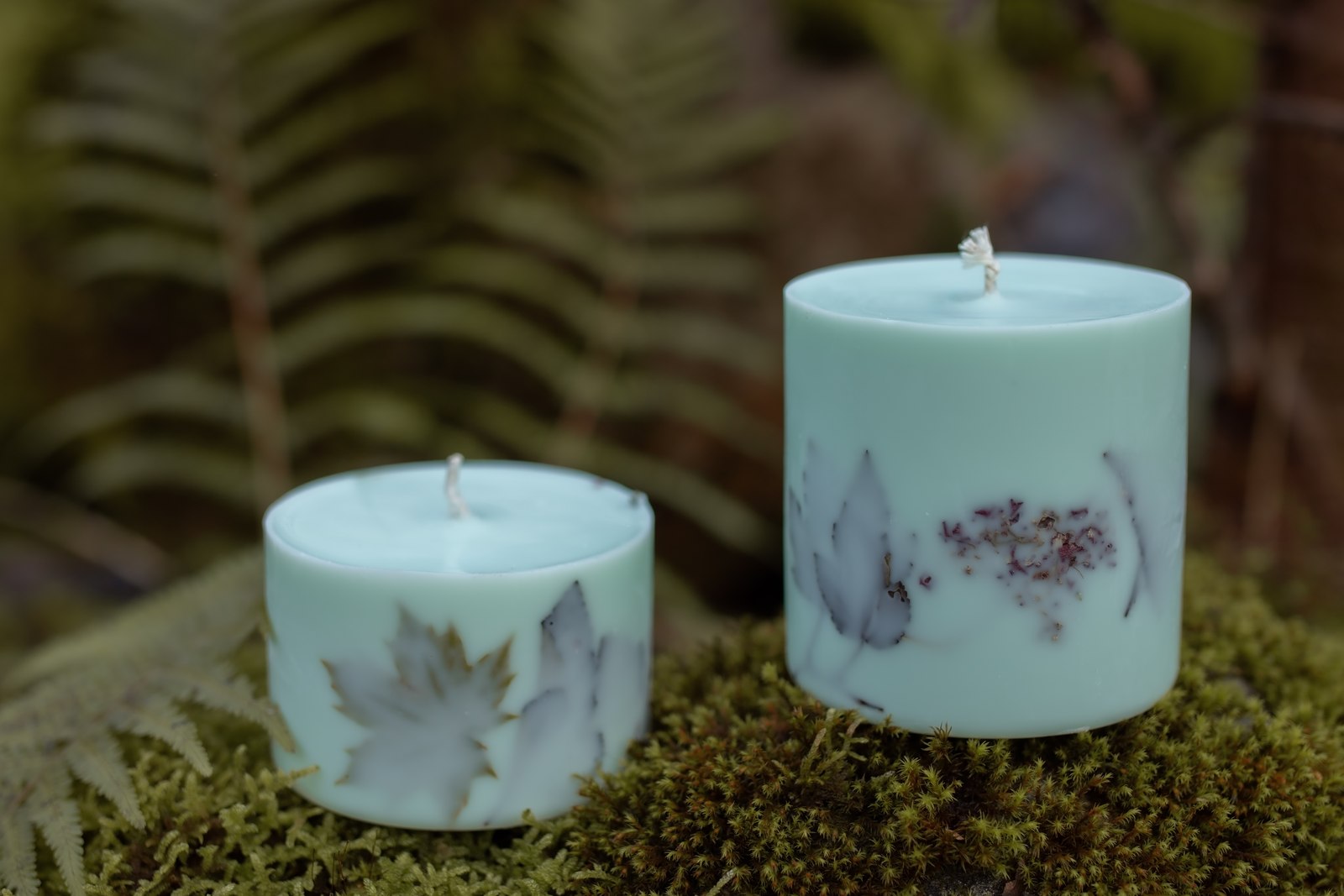 Two light-coloured TL Candles candles with botanical decorations on moss