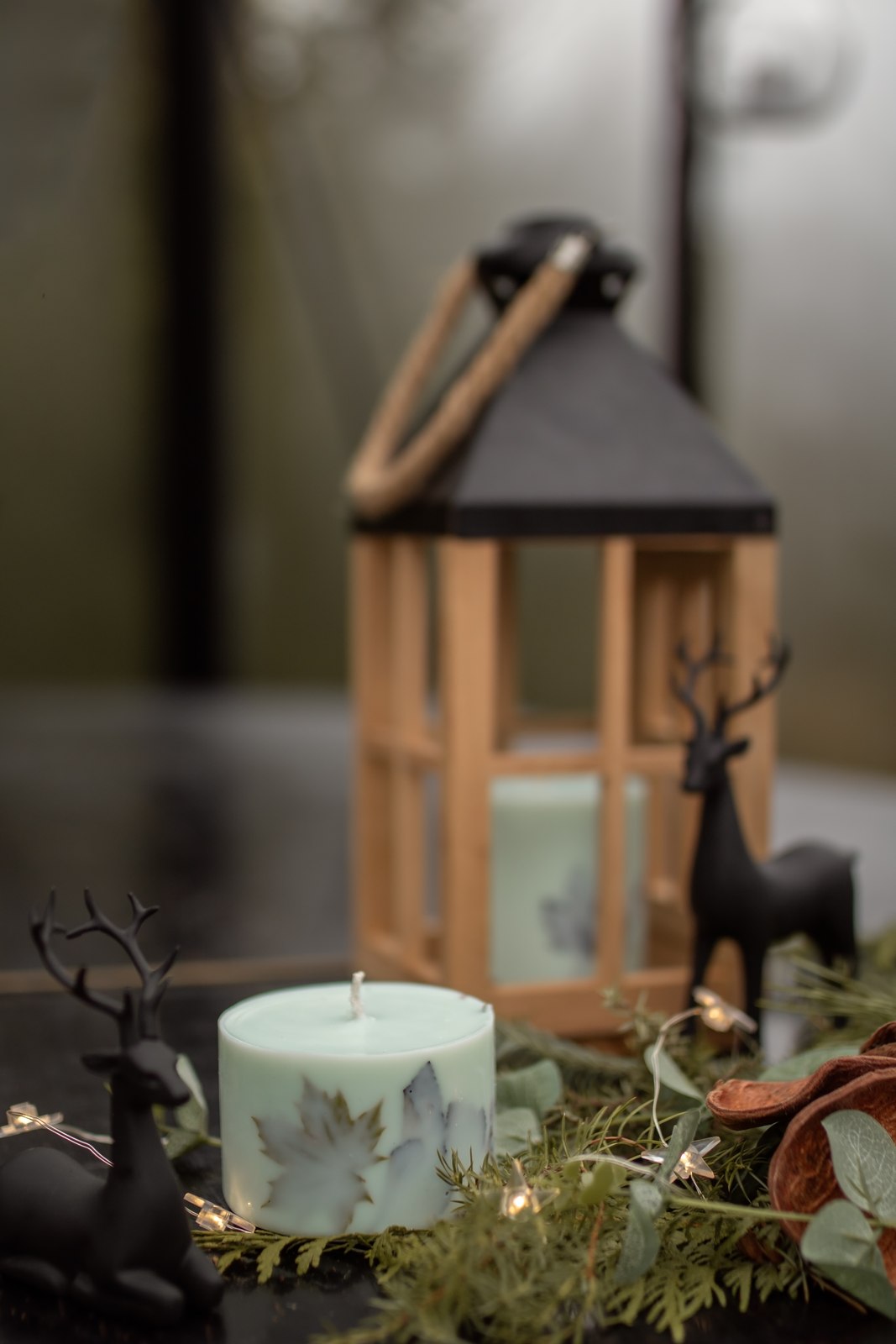 A light-coloured TL Candles candle beside a wooden lantern and greenery